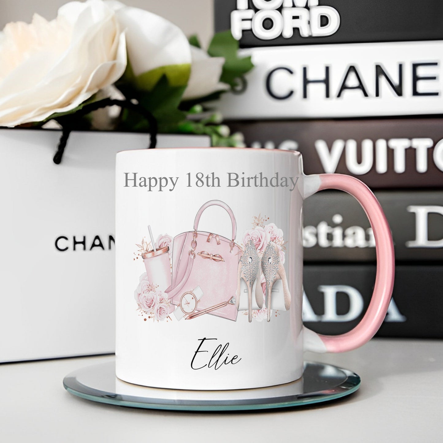 Mug with 'Happy 18th Birthday Ellie' text and pink handbag design, placed on a surface with Chanel and Dior boxes in the background.