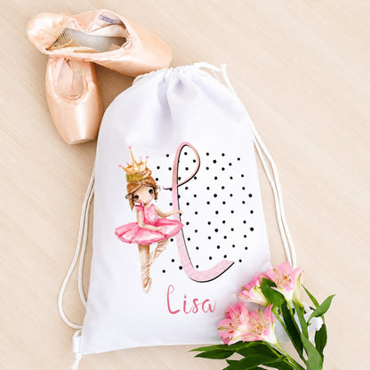 White drawstring bag with a ballerina design and the name 'Lisa', next to pink ballet shoes and flowers on a beige background.