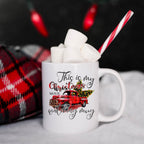 White mug with Christmas-themed design, filled with hot chocolate and marshmallows, against a dark background.