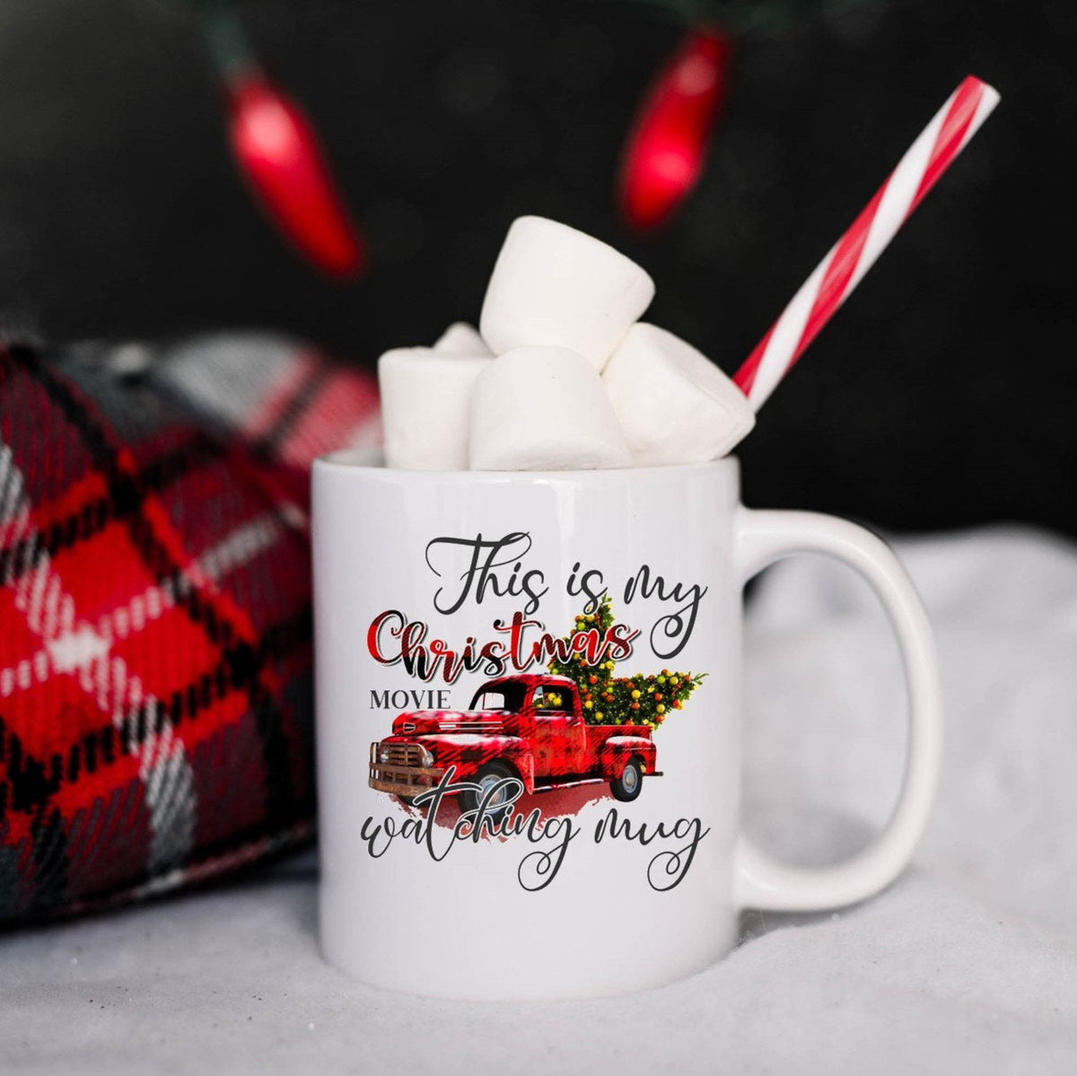 White mug with Christmas-themed design, filled with hot chocolate and marshmallows, against a dark background.