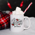 White mug with hot chocolate and marshmallows, featuring a decorative label, against a festive background.