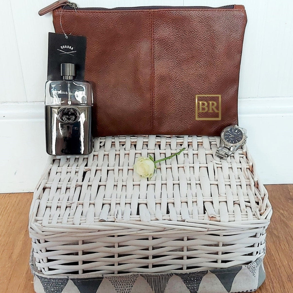 Brown leather pouch, silver bottle, white basket with a rose, and watch on a wooden surface.