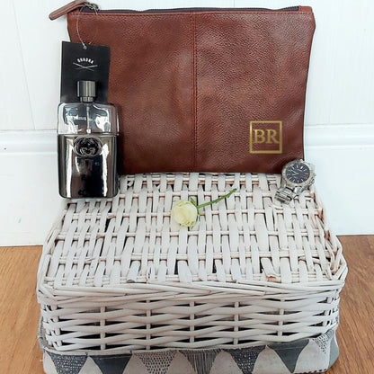 Brown leather pouch, silver bottle, white basket with a rose, and watch on a wooden surface.