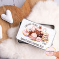 Personalized Christmas treats tin with decorative text and illustrations on a soft surface.