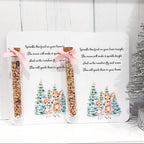 Two packages of birdseed with a deer design on a white background, next to a small decorated Christmas tree.