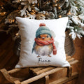 Decorative pillow with a robin design placed on a wooden surface with a Christmas tree in the background. 