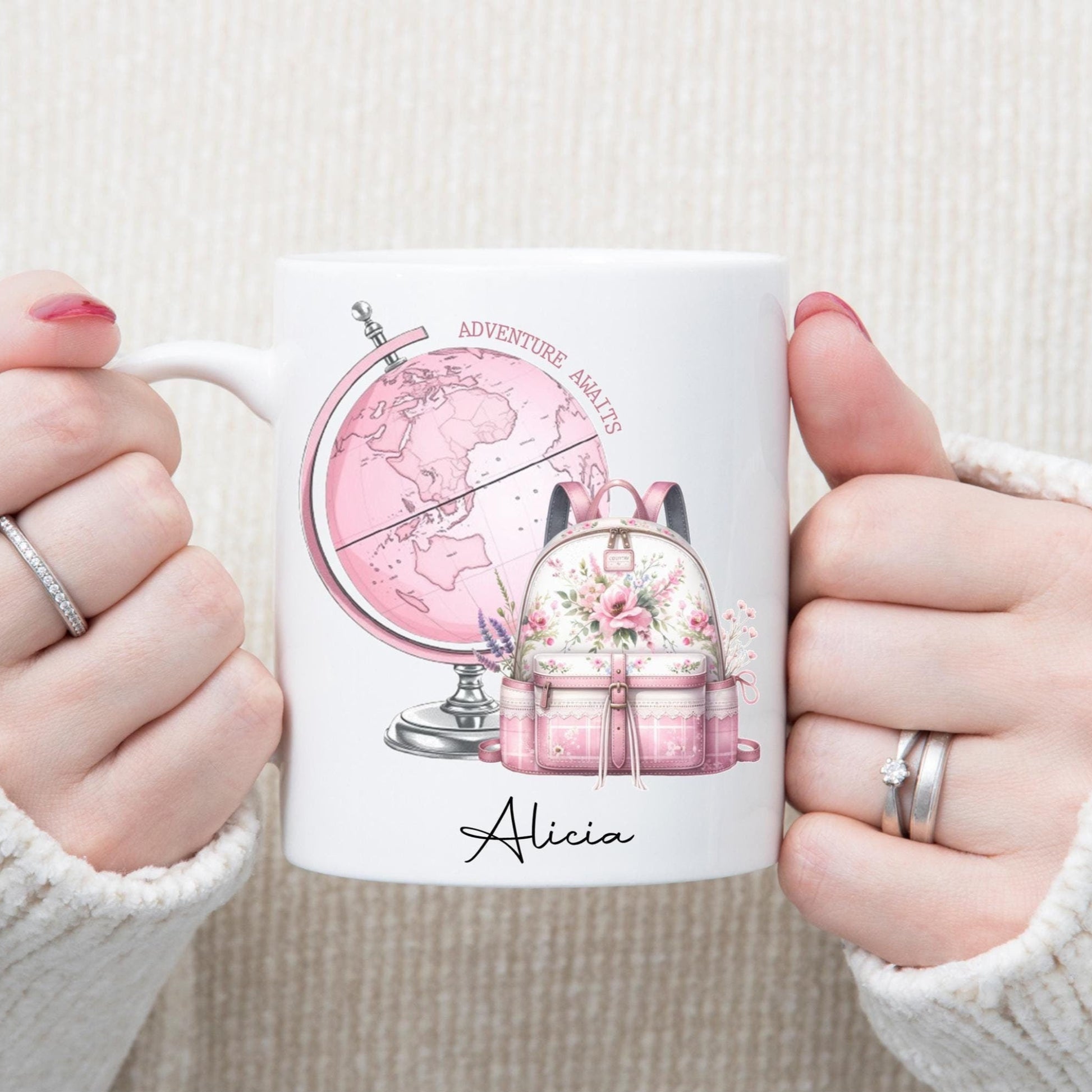 A person holding a white ceramic mug with a pink globe and rucksack design, and the name 'Alicia' printed on the mug.