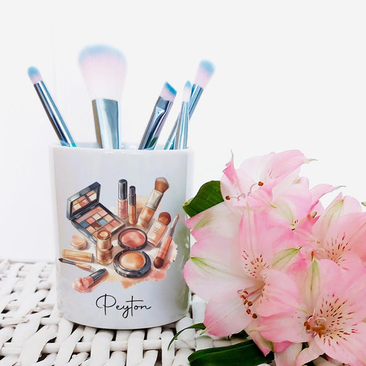 Makeup brushes in a container with 'Peyton' branding, next to pink flowers on a white background