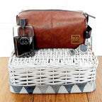 Brown leather toiletry bag with a glass and other items in a white wicker basket on a wooden surface.