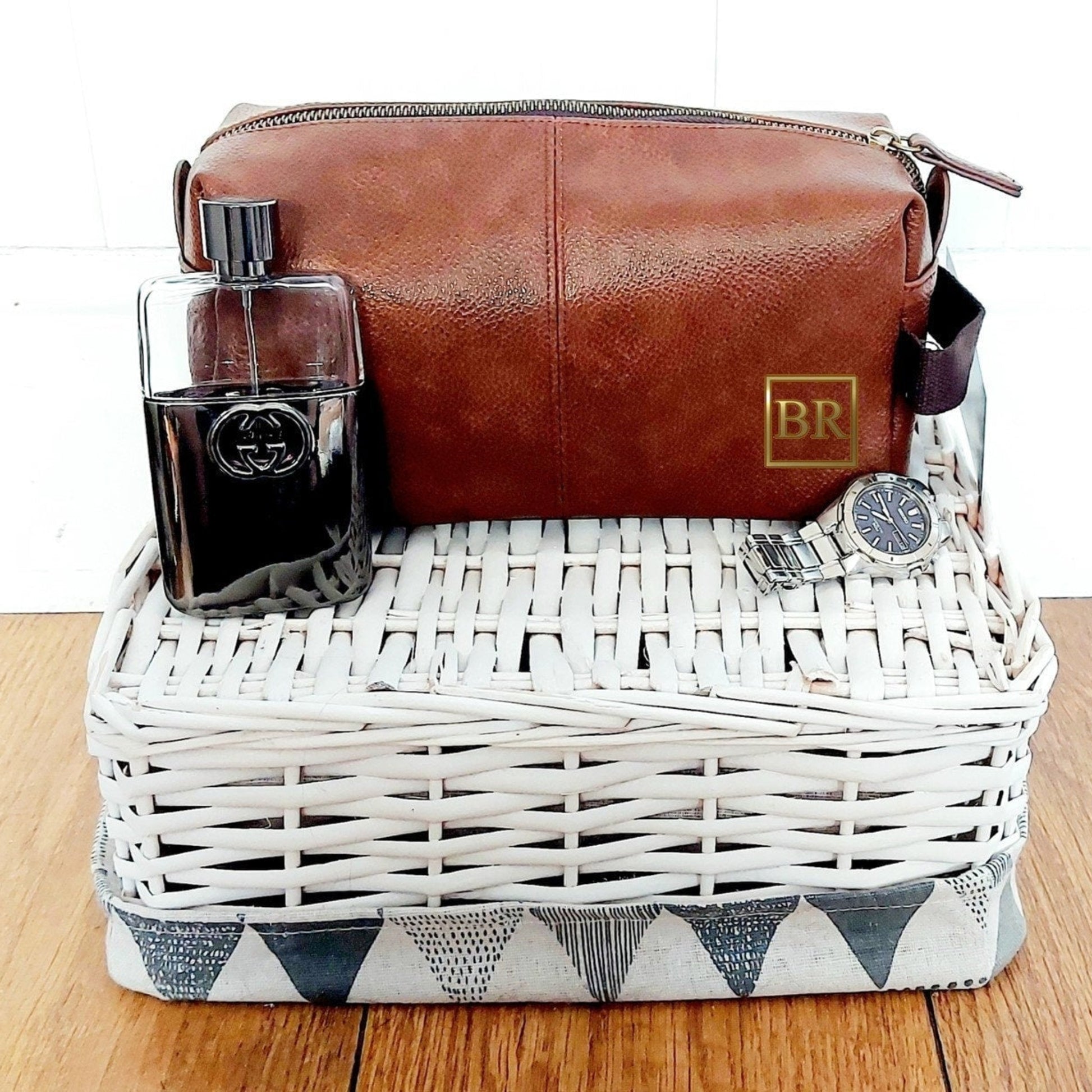 Brown leather toiletry bag with a glass and other items in a white wicker basket on a wooden surface.